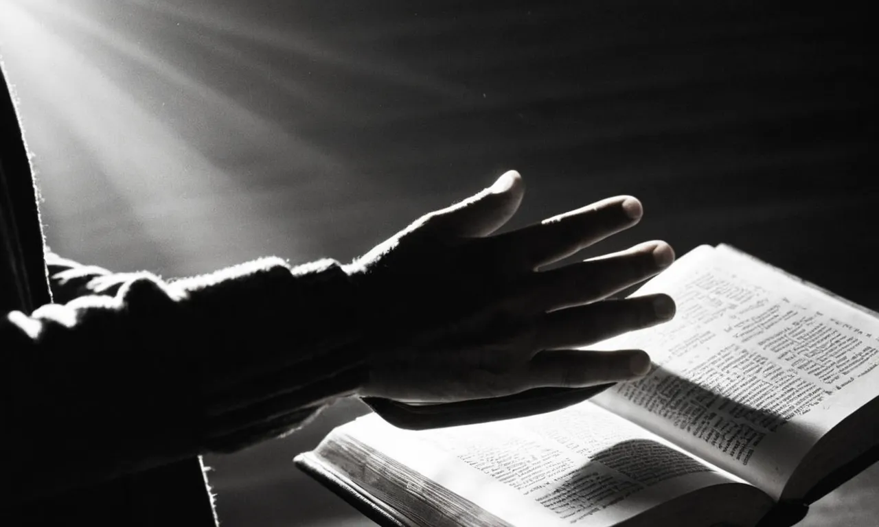 A black-and-white photo capturing an outstretched hand, holding a Bible open to the verse on theft, faintly illuminated by a single ray of light amidst darkened surroundings.