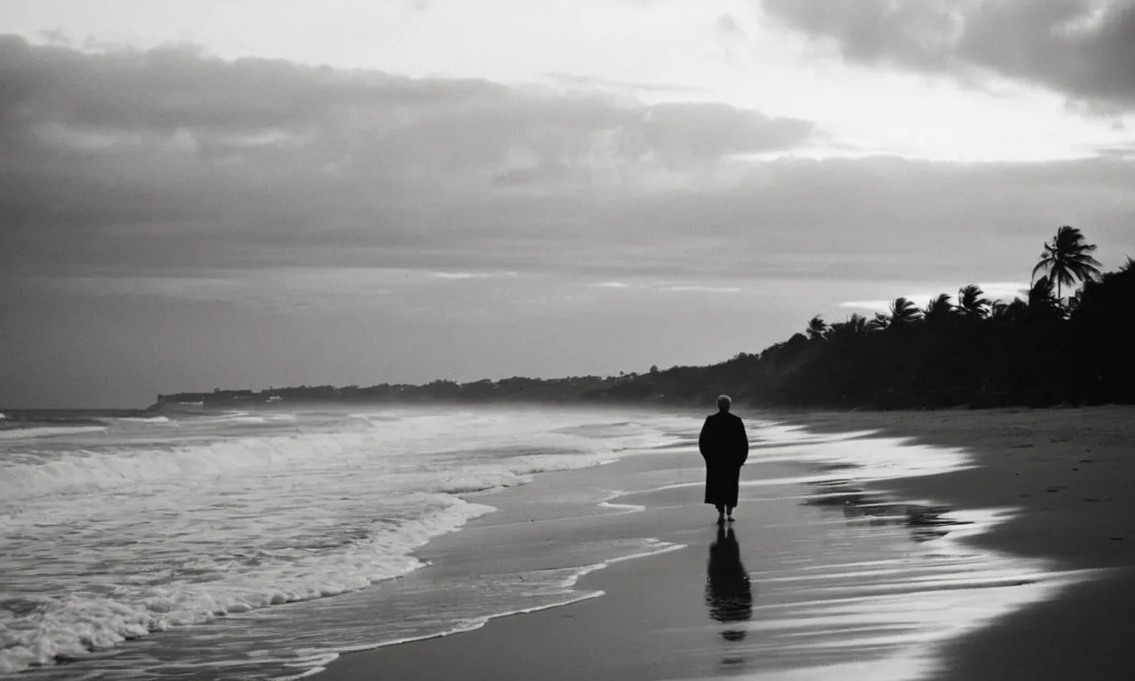 A black and white photo captures a serene beach at sunrise, with a solitary figure walking towards the horizon, symbolizing Thomas the Apostle's journey towards meeting Jesus.