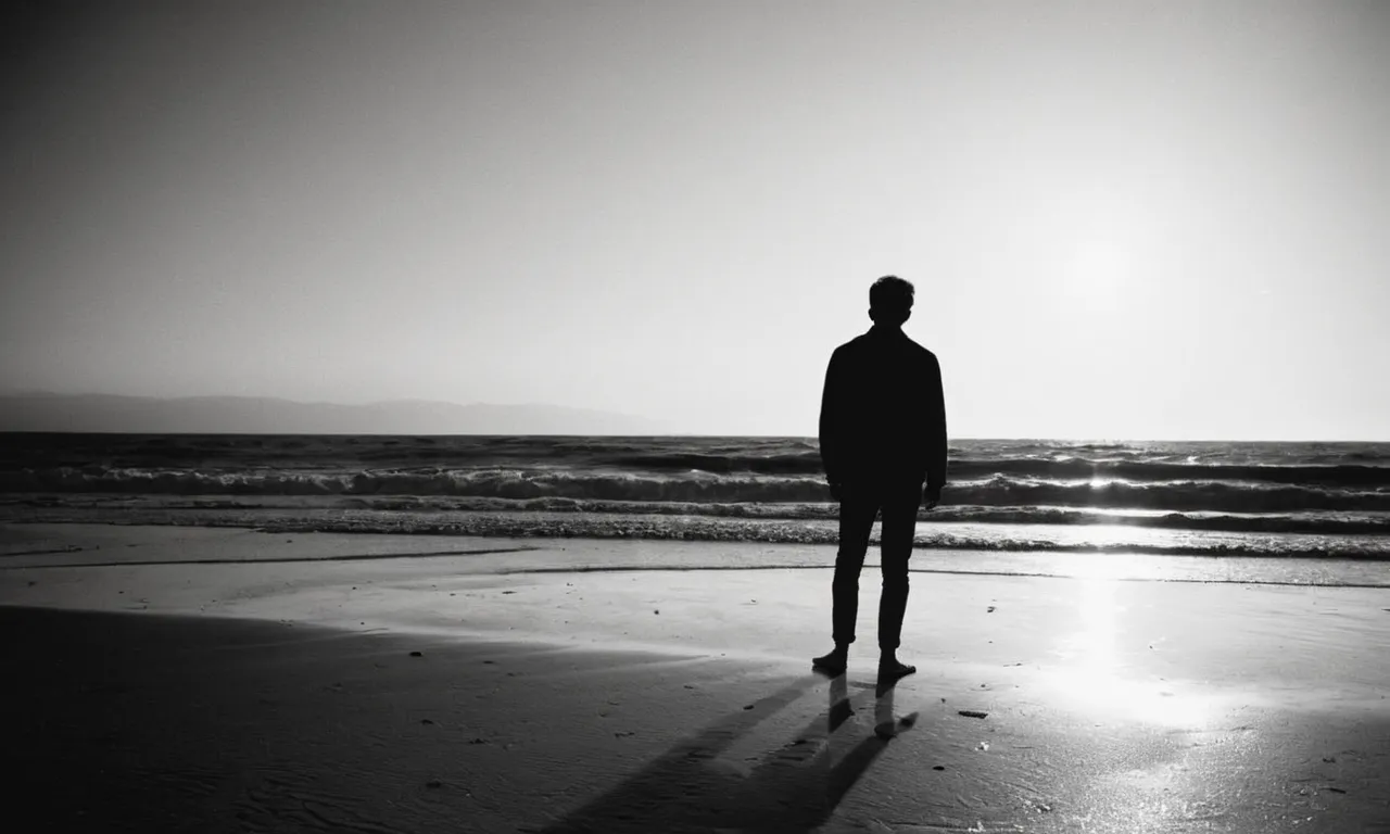 A tender black-and-white image capturing a person standing alone on a desolate beach, their silhouette framed by the setting sun, symbolizing the healing and solace that God brings to a broken heart after a lost relationship.
