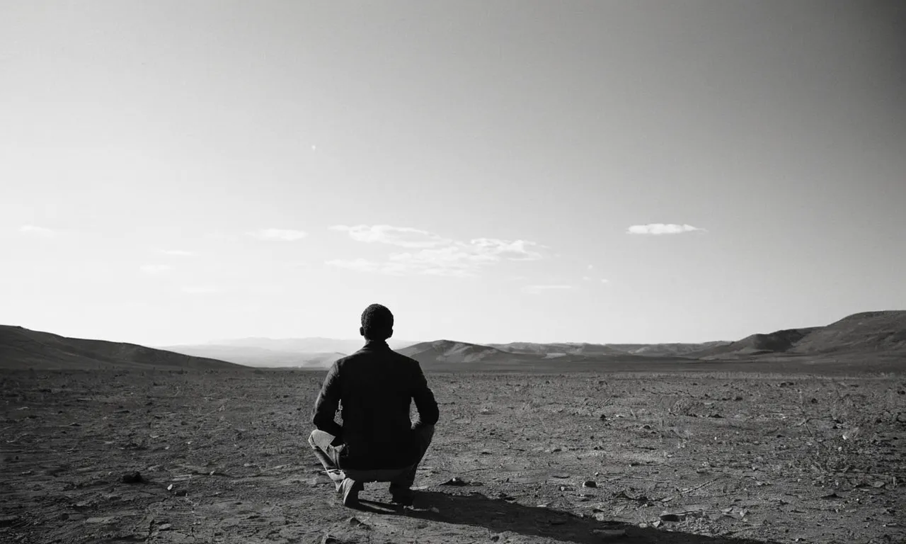 A black and white photo capturing a man kneeling in a desolate landscape, his hands raised in desperation towards the heavens, reflecting the profound anguish of Job questioning God's purpose.