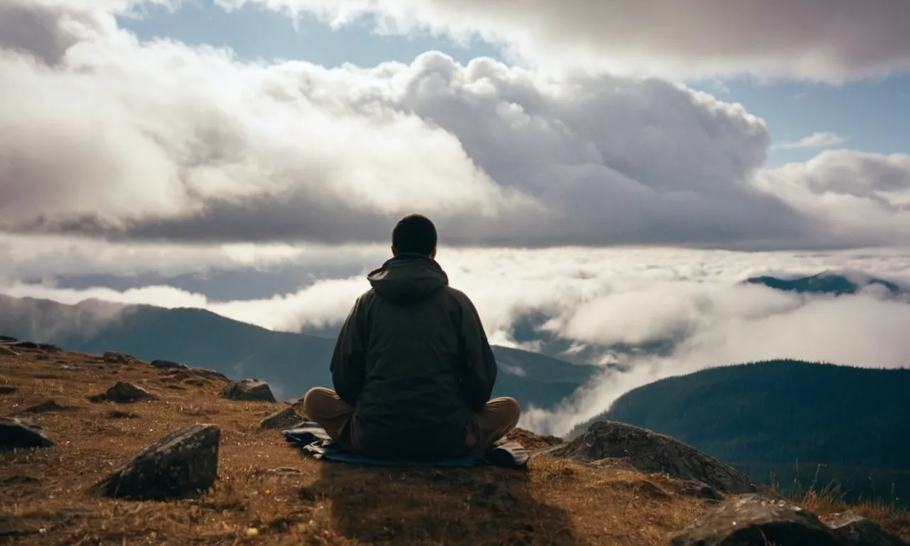 A serene image of a person sitting cross-legged on a mountaintop, eyes closed, surrounded by misty clouds. The photo captures the stillness and solitude necessary to quiet the mind and open up to hear the divine presence of God.