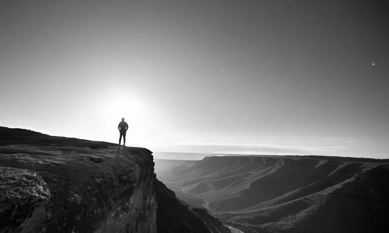 A captivating black and white image of a person standing at the edge of a cliff, gazing at a breathtaking sunrise, capturing the profound sense of awe and wonder, evoking the search for divinity.