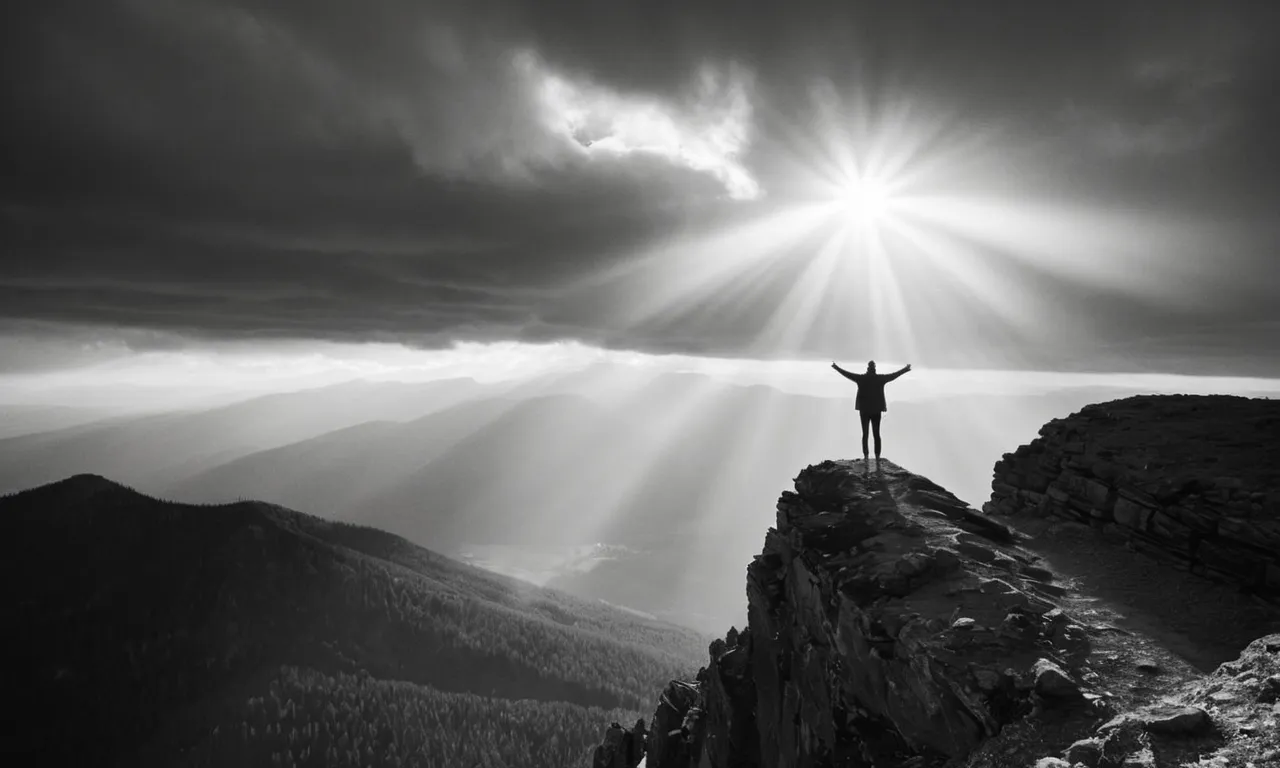 A black and white image of a solitary figure standing on a mountaintop, arms outstretched towards the heavens, as rays of light break through the clouds, creating an ethereal atmosphere.