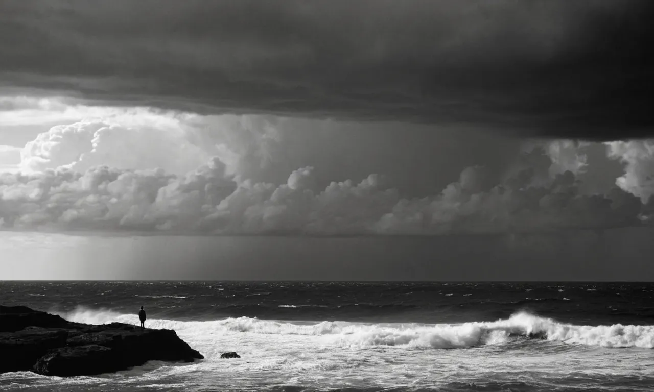 A black and white image of a solitary figure standing at the edge of a vast ocean, gazing upwards at a stormy sky, evoking the eternal question: How was God born?