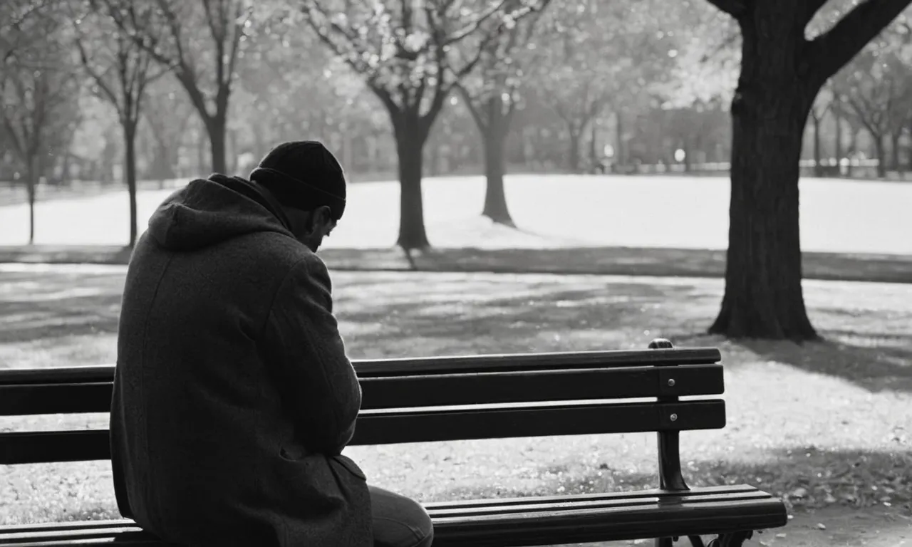 A black and white photograph captures a solitary man sitting on a park bench, his head bowed in remorse as a teardrop cascades down his cheek, echoing the pain caused by his actions.
