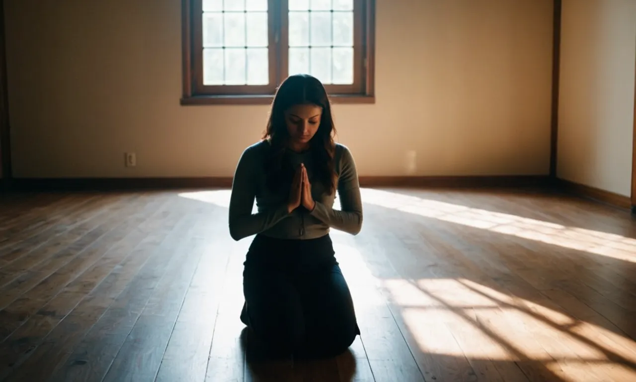 A photo of a person kneeling in a dimly lit room, eyes closed and hands clasped, as rays of sunlight stream through a window, symbolizing the power and connection found in praying out loud.