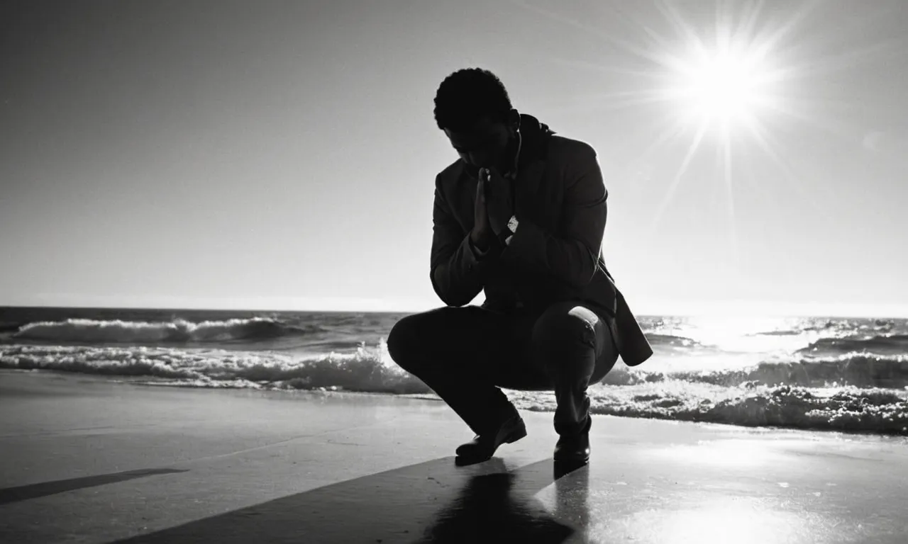 A black and white photo capturing a person kneeling before a vast ocean, arms outstretched, their face illuminated by a ray of sunlight, symbolizing a personal connection to God's infinite power and presence.
