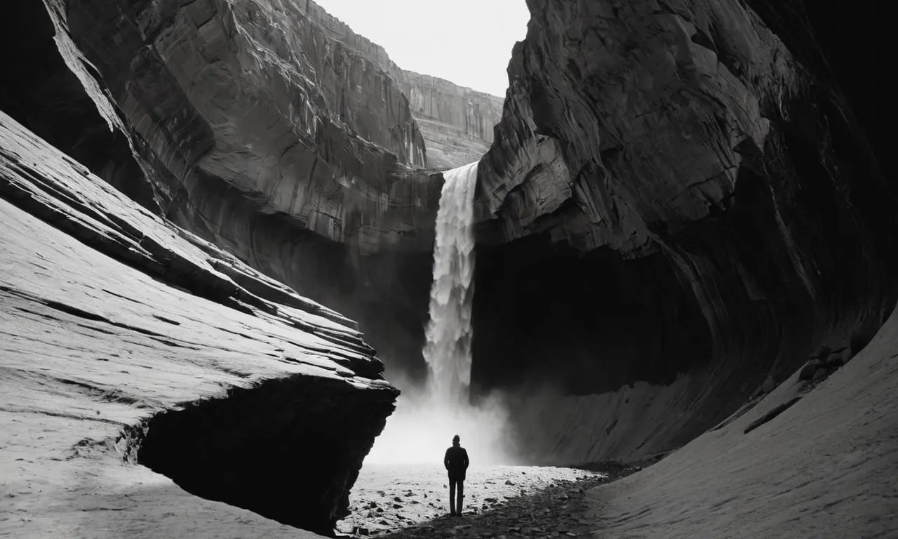 A black and white image captures a solitary figure standing at the edge of a vast chasm, symbolizing the existential divide between humanity and the divine, evoking contemplation and introspection.