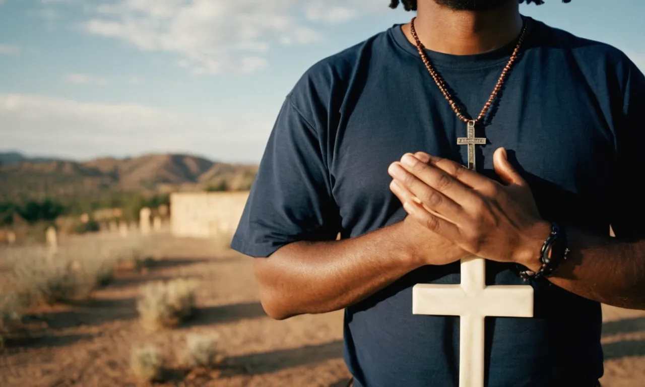 A photo capturing a person wearing a "What Would Jesus Do" shirt, their hands clasped in prayer, standing in front of a cross, radiating faith and devotion.