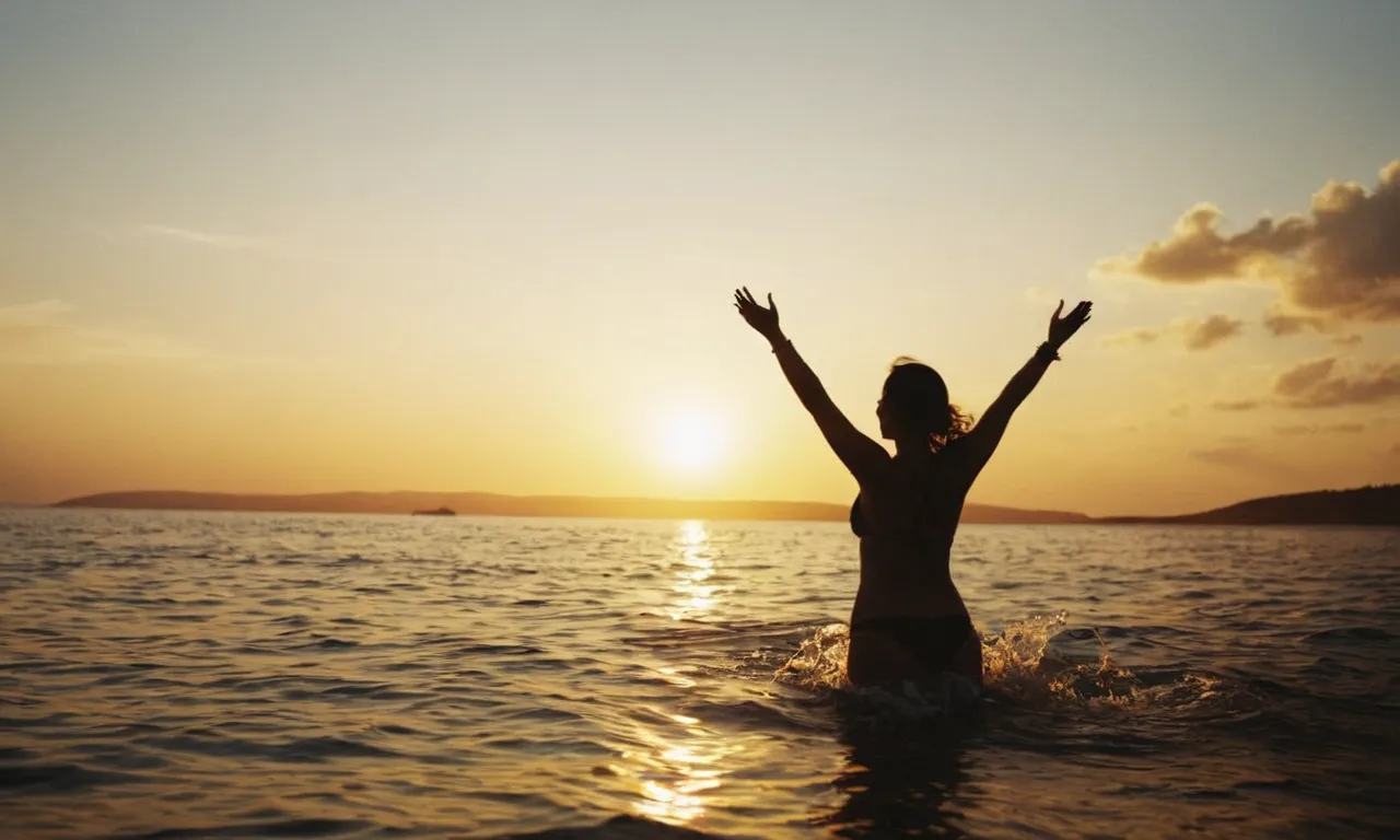 A silhouette of a person with outstretched arms, bathed in golden light, standing at the edge of a serene ocean, as the sun sets and casts a heavenly glow over the water.