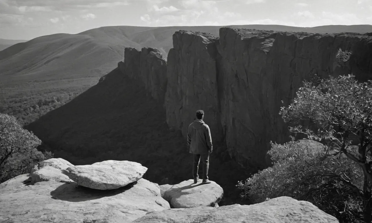 A black and white photo captures a serene landscape with a solitary figure standing on a rocky cliff, symbolizing the enigmatic question of "who was the first human on Earth" as explored in the Bible.