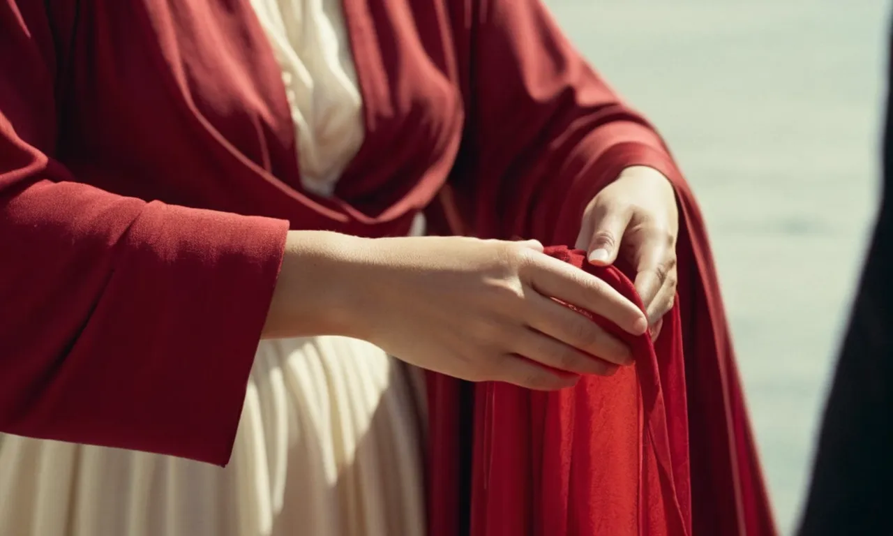 A close-up photograph capturing a hand reaching out to touch the hem of a flowing red garment, symbolizing the woman with an issue of blood who sought healing from Jesus in the Bible.