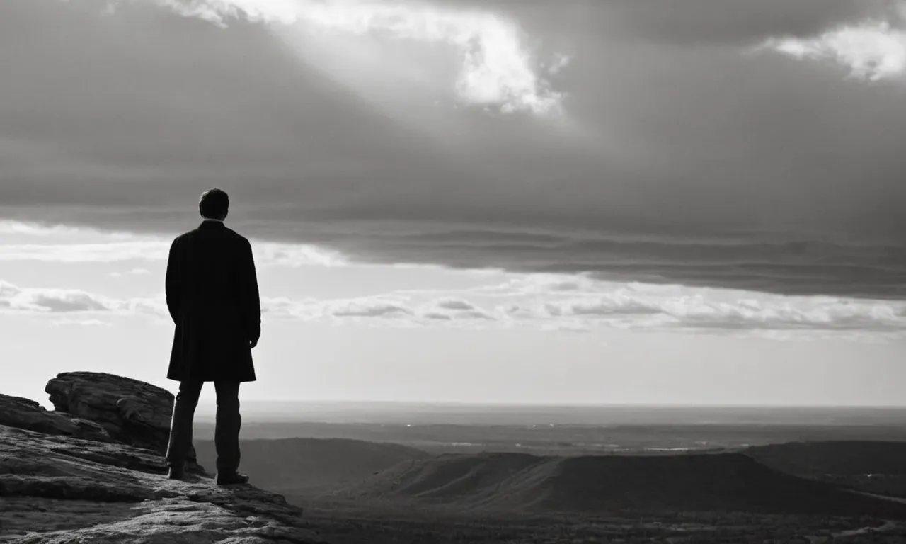 A black and white photograph captures a solitary figure standing on a cliff edge, gazing up at a vast, cloudy sky, questioning the invisible presence of God.